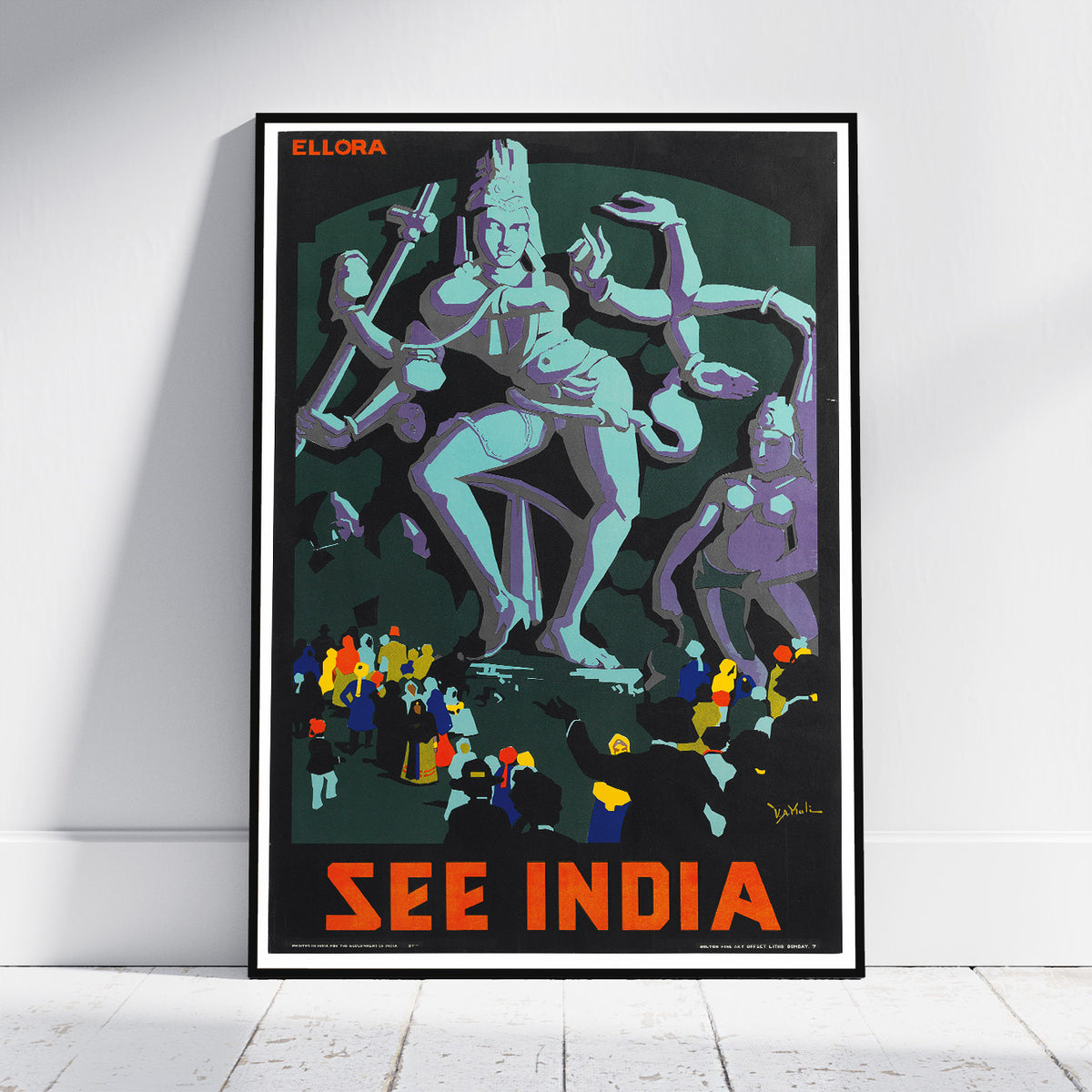 A framed travel poster of India leaning against a white wall on a light wood floor. The poster features a stylized illustration of Lord Ganesha in light blue, with other figures in purple, yellow, and blue, and bold orange text reading 'SEE INDIA' at the bottom.