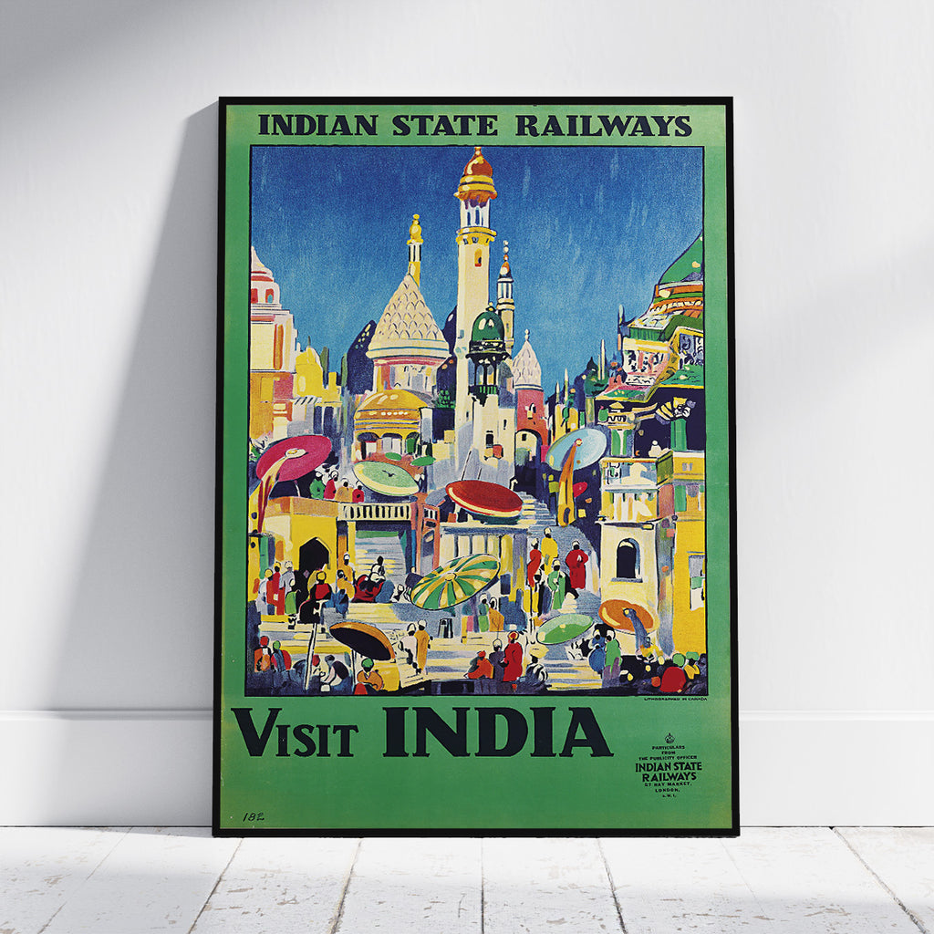 A framed vintage-style travel poster leaning against a white wall on a light floor. The poster reads 'INDIAN STATE RAILWAYS' at the top and 'VISIT INDIA' at the bottom, with a colorful illustration of buildings, people, and umbrellas in India.