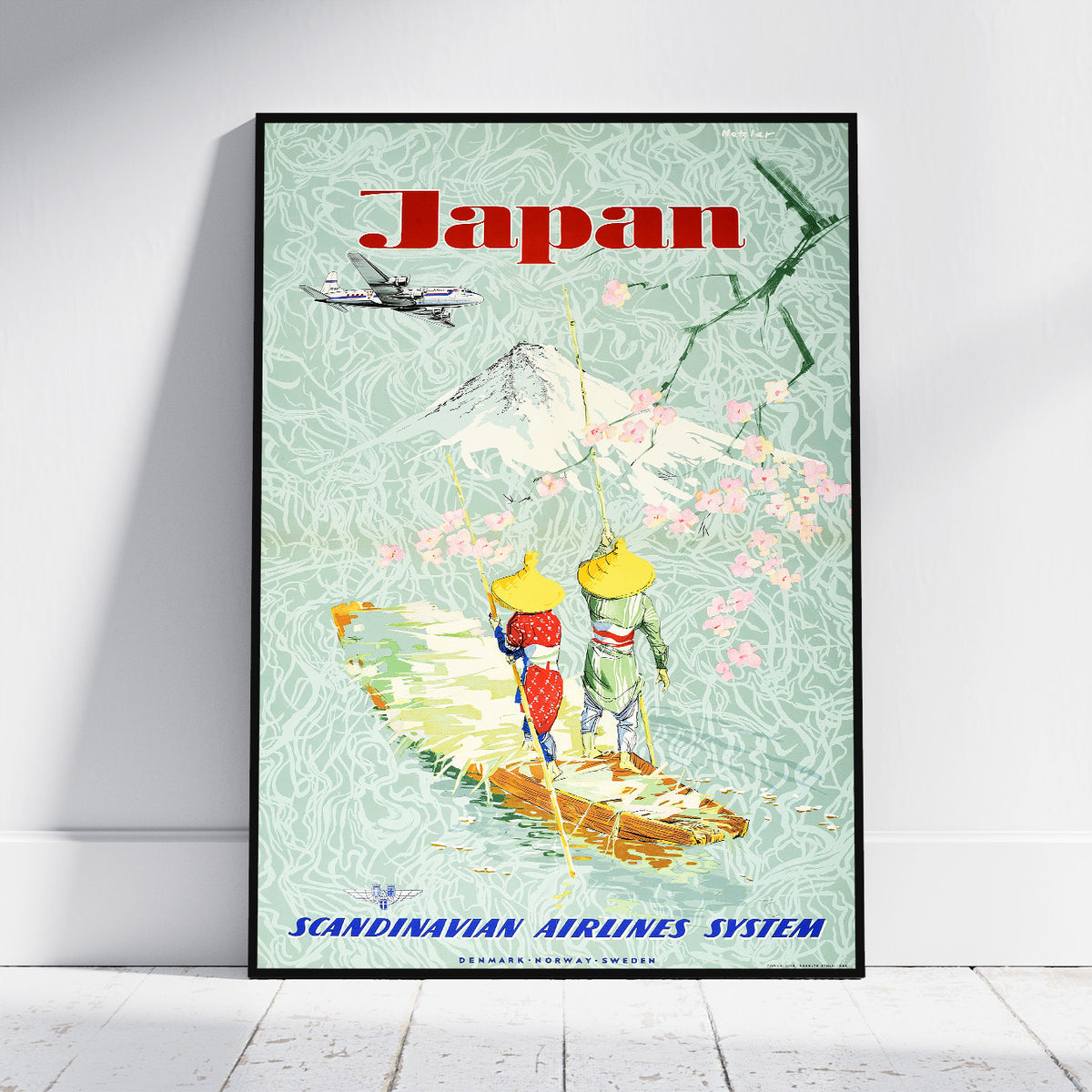A framed vintage-style travel poster leaning against a white wall on a light floor. The poster reads "Japan" at the top and "Scandinavian Airlines System" at the bottom, with an illustrated mountain, cherry blossoms, a boat, and a small airplane.