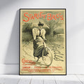 A framed vintage-style poster leaning against a white wall on a light floor. The poster reads 'Starley Bro's' and shows an illustrated woman riding a bicycle in a sepia landscape, with red and black text and a black frame around the print.