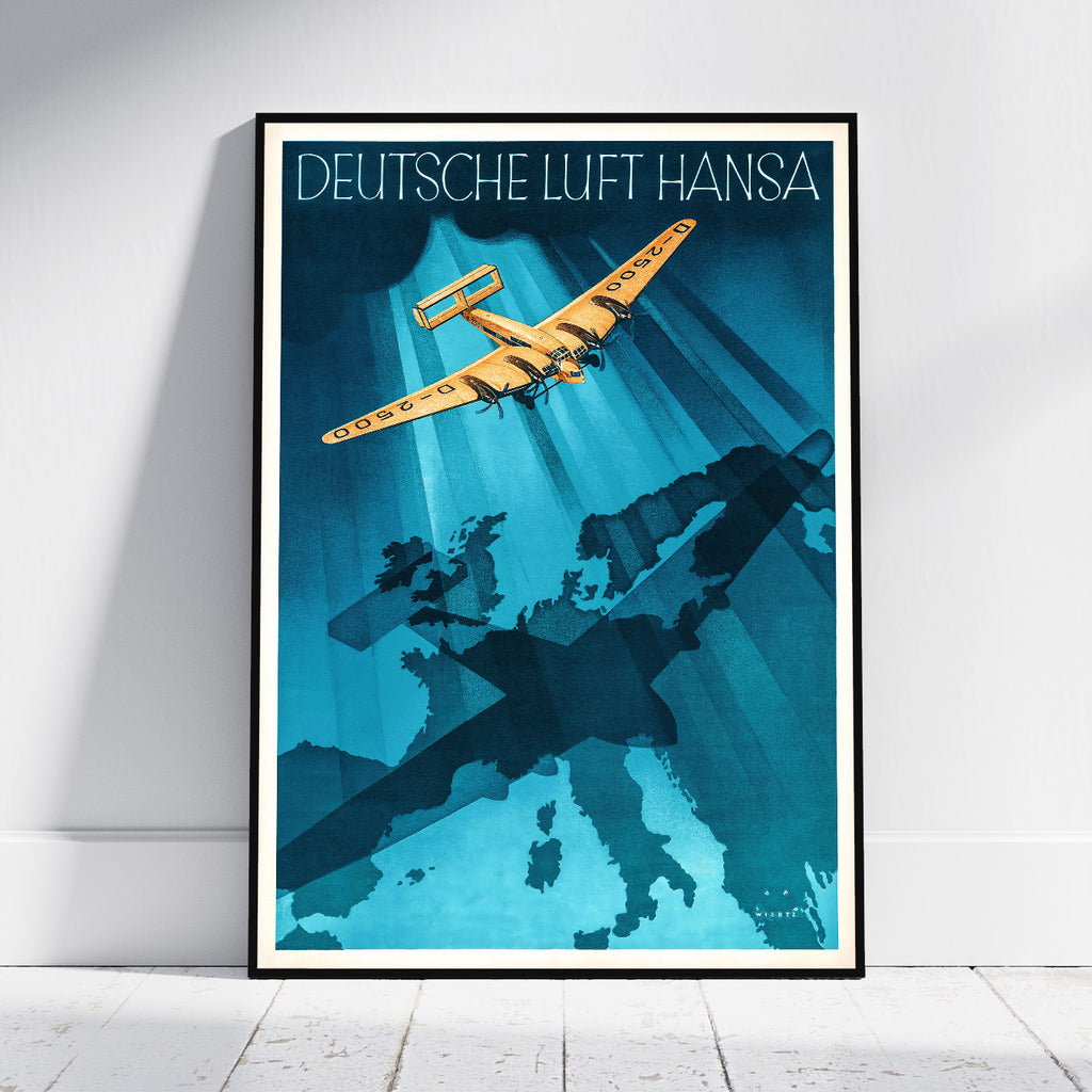 A framed vintage-style travel poster leaning against a white wall on a light floor. The poster reads 'DEUTSCHE LUFT HANSA' at the top and features a yellow airplane flying over a blue map silhouette of Germany and surrounding countries.
