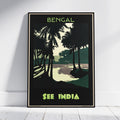 A framed travel poster leaning against a white wall on a light wood floor. The poster features a stylized illustration of palm trees and a shoreline with the text 'BENGAL' at the top and 'SEE INDIA' at the bottom in lime green.
