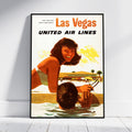 A framed vintage-style Las Vegas United Air Lines poster leaning against a white wall on a light floor. The poster shows a retro illustration of a woman by a pool with the text 'Las Vegas UNITED AIR LINES' at the top.
