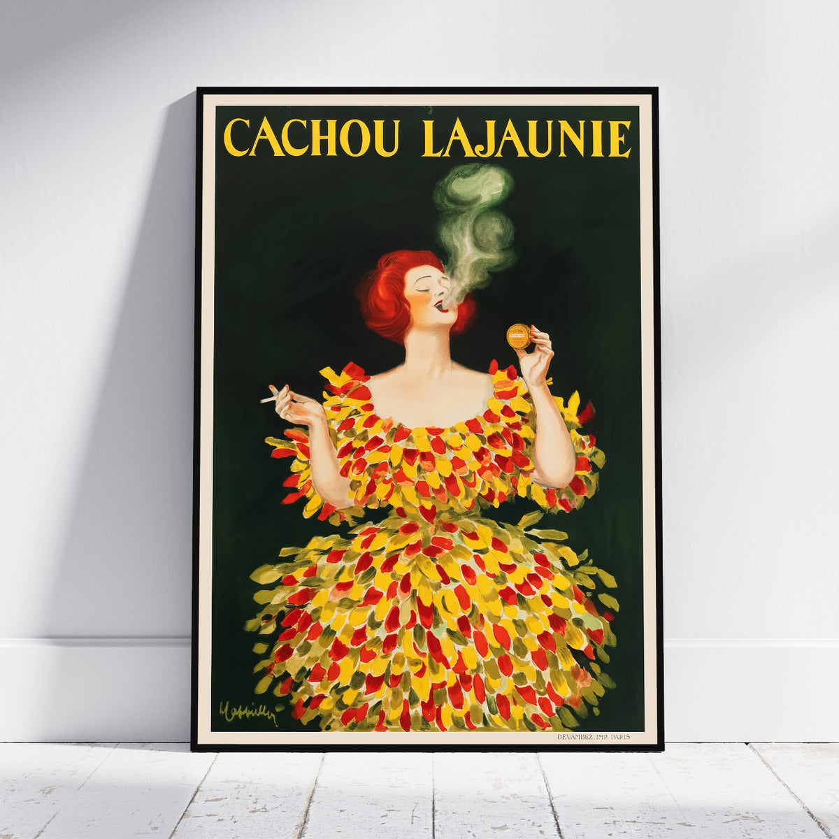 A framed vintage-style poster leaning against a white wall on a light floor. The poster shows a woman with red hair wearing a dress made of yellow and red leaves, smoking a cigarette, with the text 'CACHOU LAJAUNIE' at the top.