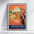 A framed vintage-style travel poster leaning against a white wall on a light floor. The poster depicts a colorful scene with a large white domed building, figures near water, and bold text at the bottom in Bengali and English.