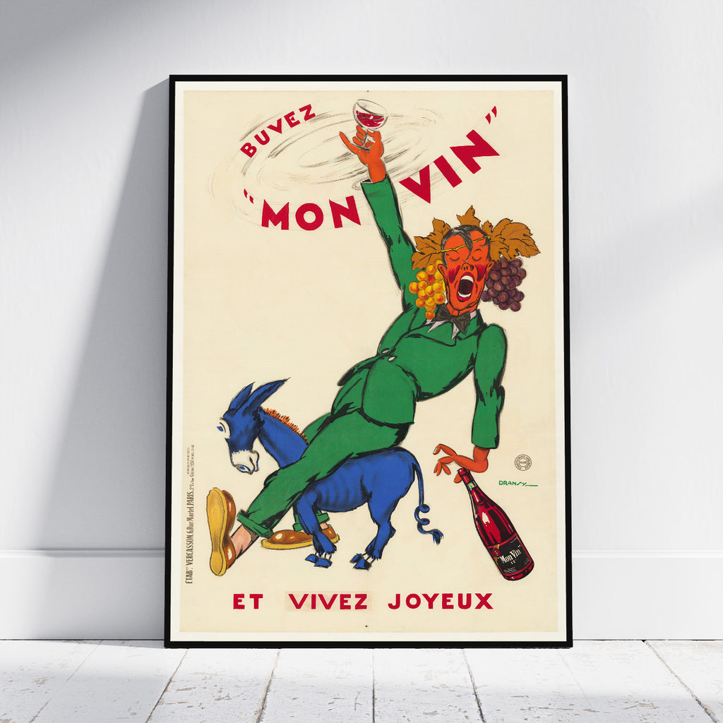 A framed vintage French poster leaning against a white wall on a light floor. The poster features a stylized red-faced figure in a green suit riding a blue donkey while holding a wine glass and a wine bottle, with the text “Buevez Mon Vin” and “Et Vivez Joyeux.
