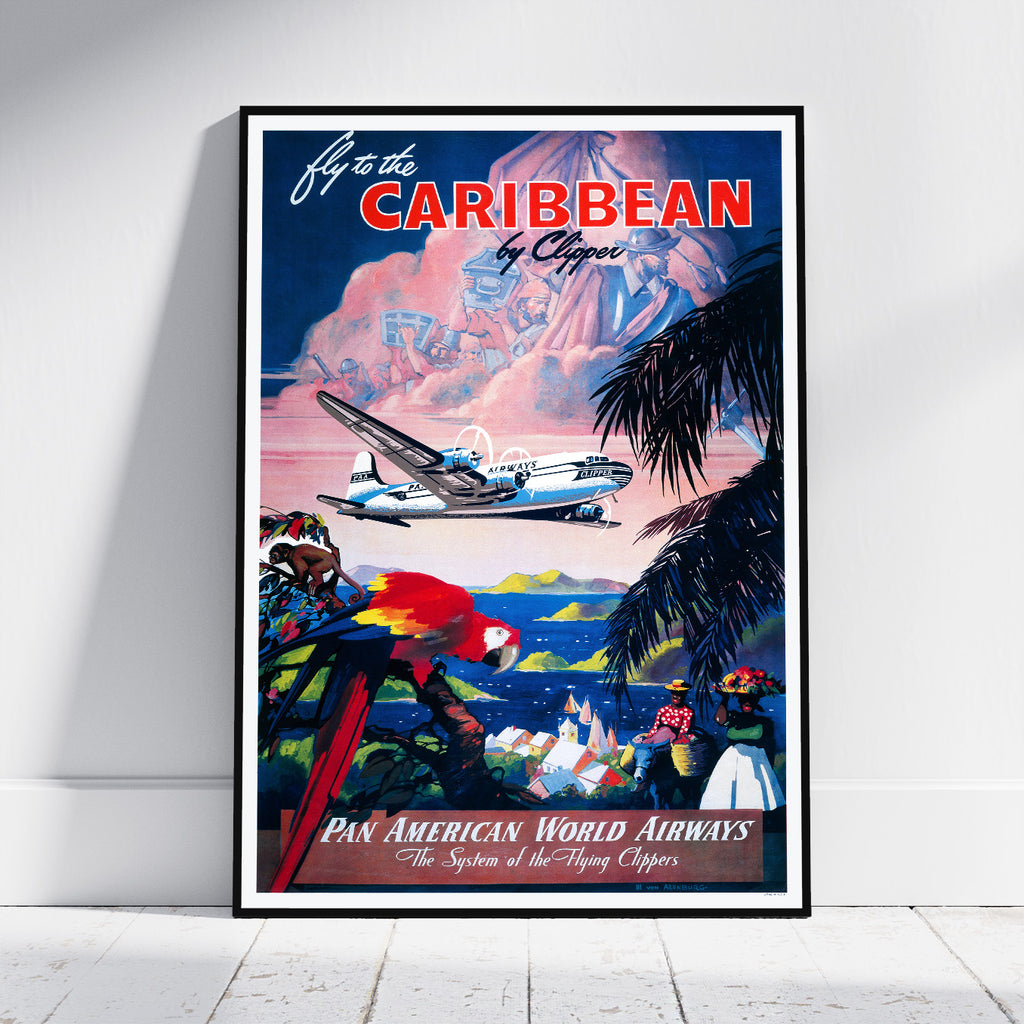 A framed vintage-style travel poster leaning against a white wall on a light floor. The poster reads 'Fly to the CARIBBEAN by Ocean' and 'Pan American World Airways' with an illustration of a retro airplane, palm trees, a red-and-yellow parrot, and people by the ocean.