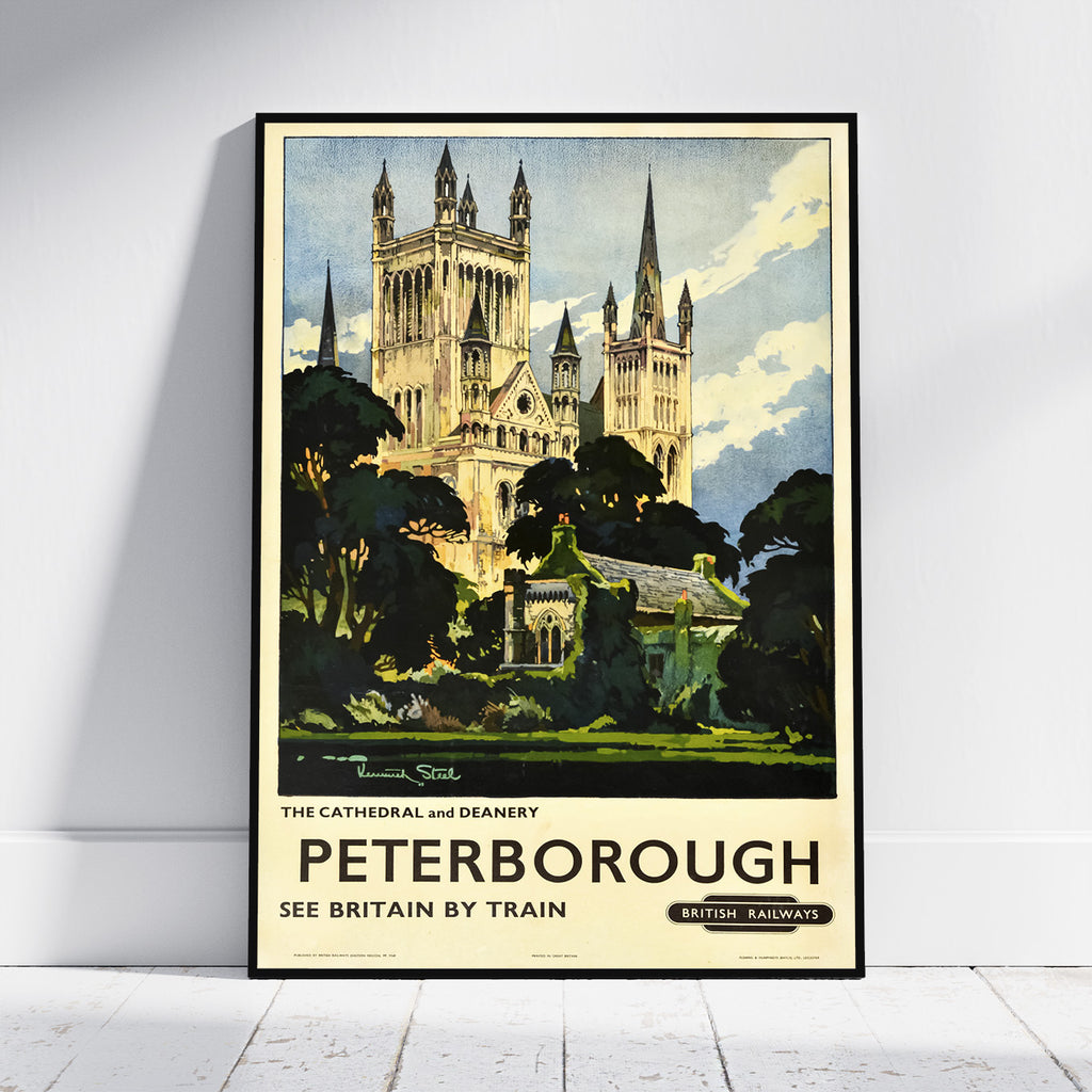A framed vintage travel poster of Peterborough, England, leaning against a white wall on a light wood floor. The poster features an illustration of the cathedral and surrounding greenery, with the text 'PETERBOROUGH SEE BRITAIN BY TRAIN' and 'British Railways'.
