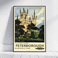 A framed vintage travel poster of Peterborough, England, leaning against a white wall on a light wood floor. The poster features an illustration of the cathedral and surrounding greenery, with the text 'PETERBOROUGH SEE BRITAIN BY TRAIN' and 'British Railways'.