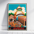 A framed vintage-style travel poster of Calcutta's cathedral, leaning against a white wall on a light wood floor. The poster features a colorful illustration of the cathedral dome, surrounding historic buildings, and people in the foreground under a bright blue sky, with the word 'Calcutta' printed in red at the bottom.