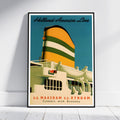 A framed vintage-style travel poster leaning against a white wall on a light wood floor. The poster shows a large ship with a yellow and green striped funnel, cream-colored hull, and blue sky background.