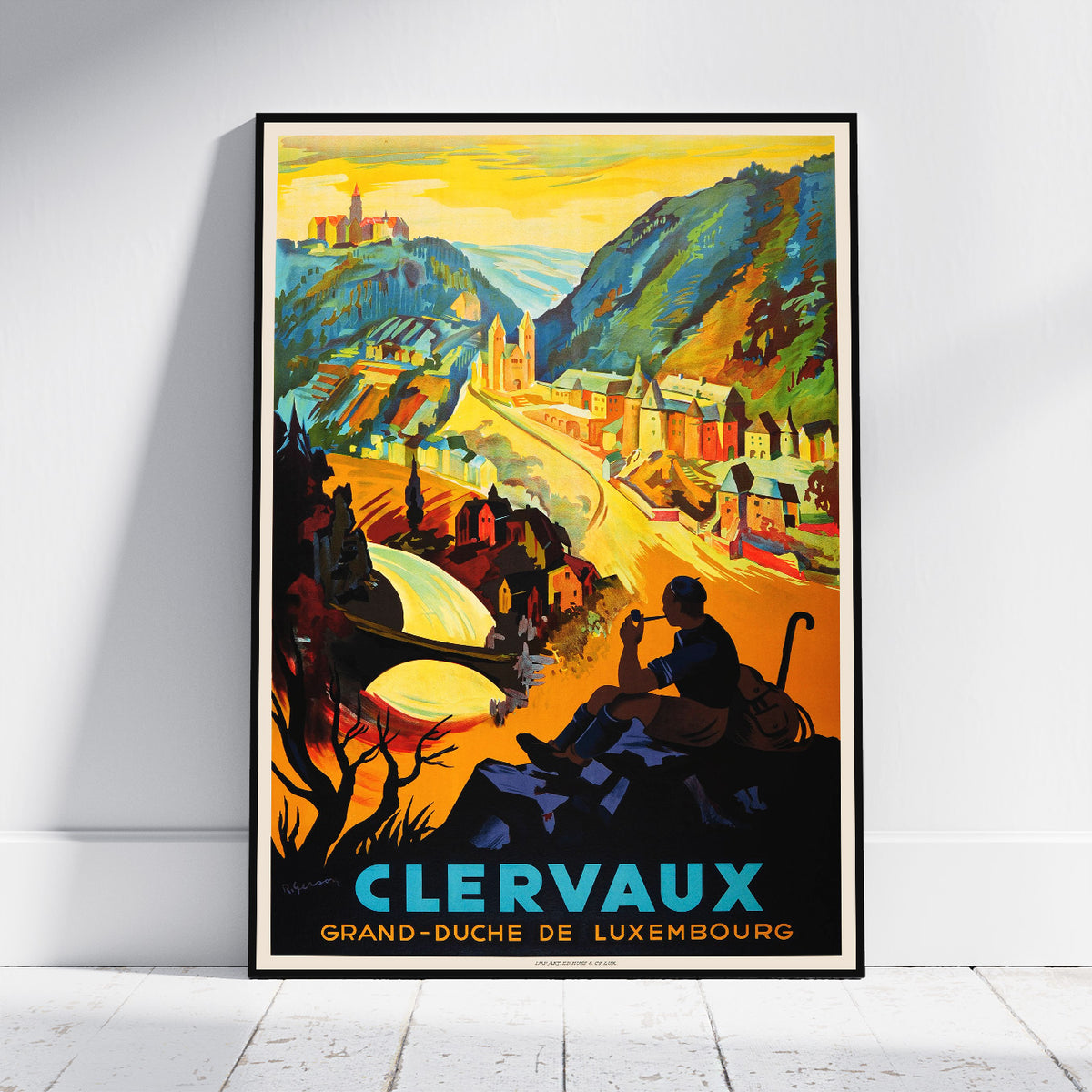 A framed vintage-style travel poster leaning against a white wall on a light wood floor. The poster depicts a scenic mountain town with the text 'CLERVAUX GRAND-DUCHE DE LUXEMBOURG' in large blue and yellow lettering at the bottom.