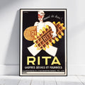 A framed vintage-style poster leaning against a white wall on a light floor. The poster shows a chef holding waffles with the large text 'RITA' and additional French text, with a black background and yellow lettering.