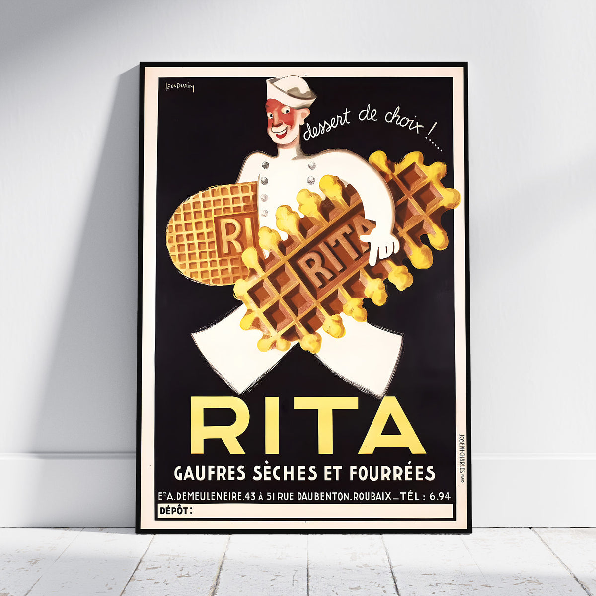A framed vintage-style poster leaning against a white wall on a light floor. The poster shows a chef holding waffles with the large text 'RITA' and additional French text, with a black background and yellow lettering.