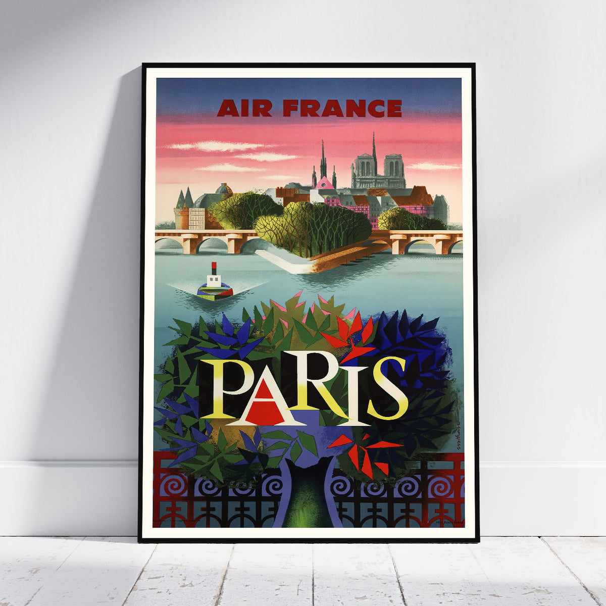 A framed vintage-style Paris travel poster leaning against a white wall on a light floor. The poster features the text 'AIR FRANCE' at the top and 'PARIS' in large letters over a colorful illustration of the city skyline, water, and foliage.