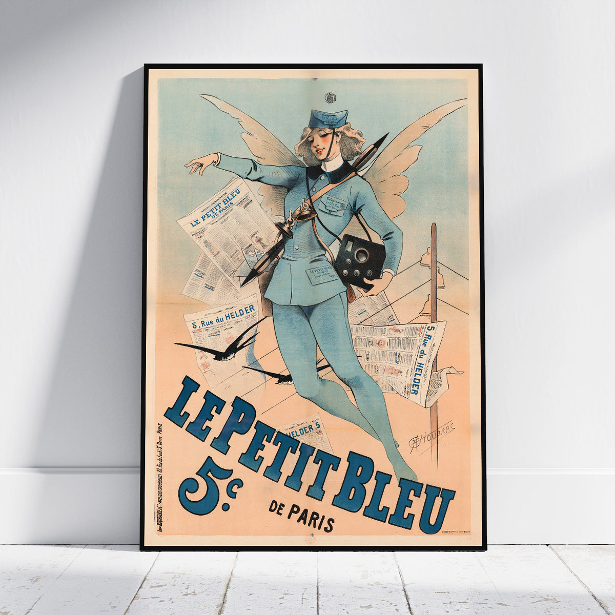 A framed vintage-style poster leaning against a white wall on a light wood floor. The poster features an illustrated woman in a blue uniform with wings, holding a rifle and a camera, with large blue text reading 'LE PETIT BLEU 5  de PARIS' on a warm cream background.