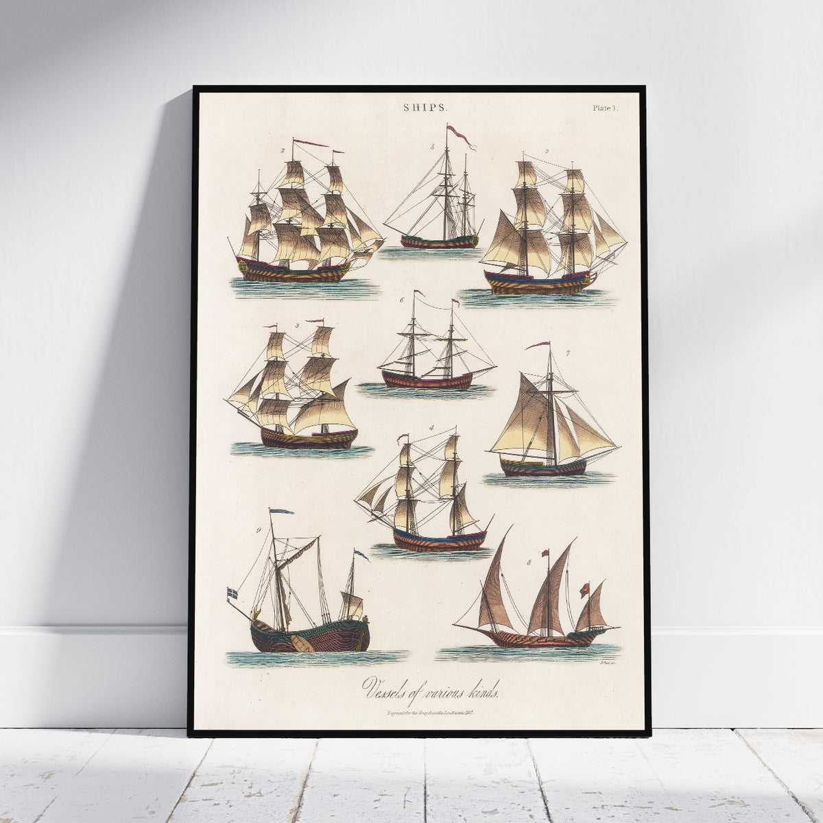 A framed vintage nautical art print featuring nine detailed illustrations of historical sailing ships on an off-white background, leaning against a white wall on a light wood floor.