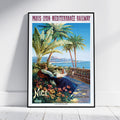 A framed vintage-style travel poster leaning against a white wall on a light floor. The poster reads 'PARIS - LYON - MÉDITERRANÉE RAILWAY' and 'Nice' with an illustrated scene of palm trees, a seaside terrace, flowers, and a woman in a blue dress.