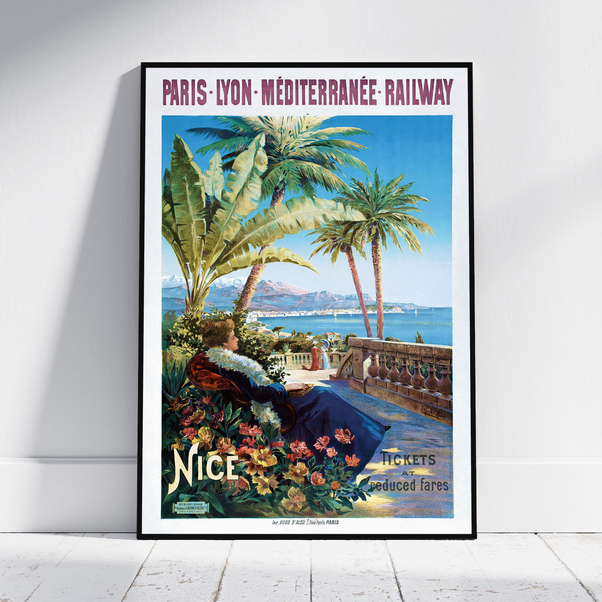 A framed vintage-style travel poster leaning against a white wall on a light floor. The poster reads 'PARIS - LYON - MÉDITERRANÉE RAILWAY' and 'Nice' with an illustrated scene of palm trees, a seaside terrace, flowers, and a woman in a blue dress.