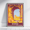 A framed vintage-style travel poster for Rome, leaning against a white wall on a light wood floor. The poster features a large stone archway in warm orange and yellow tones, with the Colosseum visible in the background under a pale blue sky.