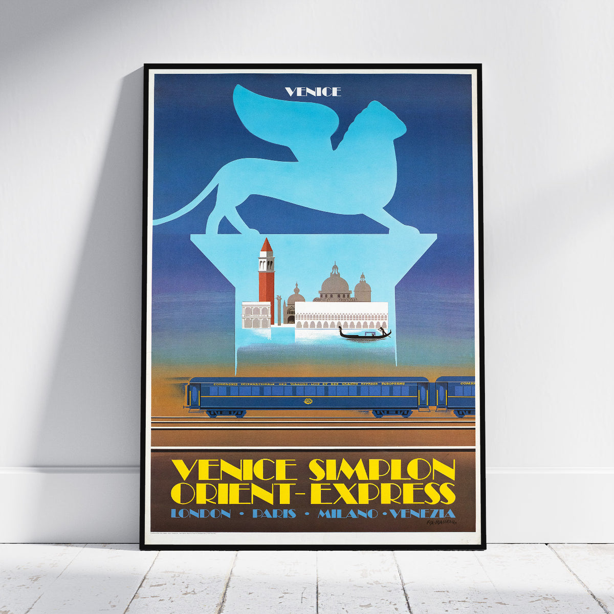 A framed vintage-style travel poster leaning against a white wall on a light wood floor. The poster features a blue winged lion silhouette above Venice landmarks, with a blue train on tracks and yellow text reading 'VENICE SIMPLON ORIENT-EXPRESS' and 'LONDRAN PARIS - MIANG - VENECIA'.