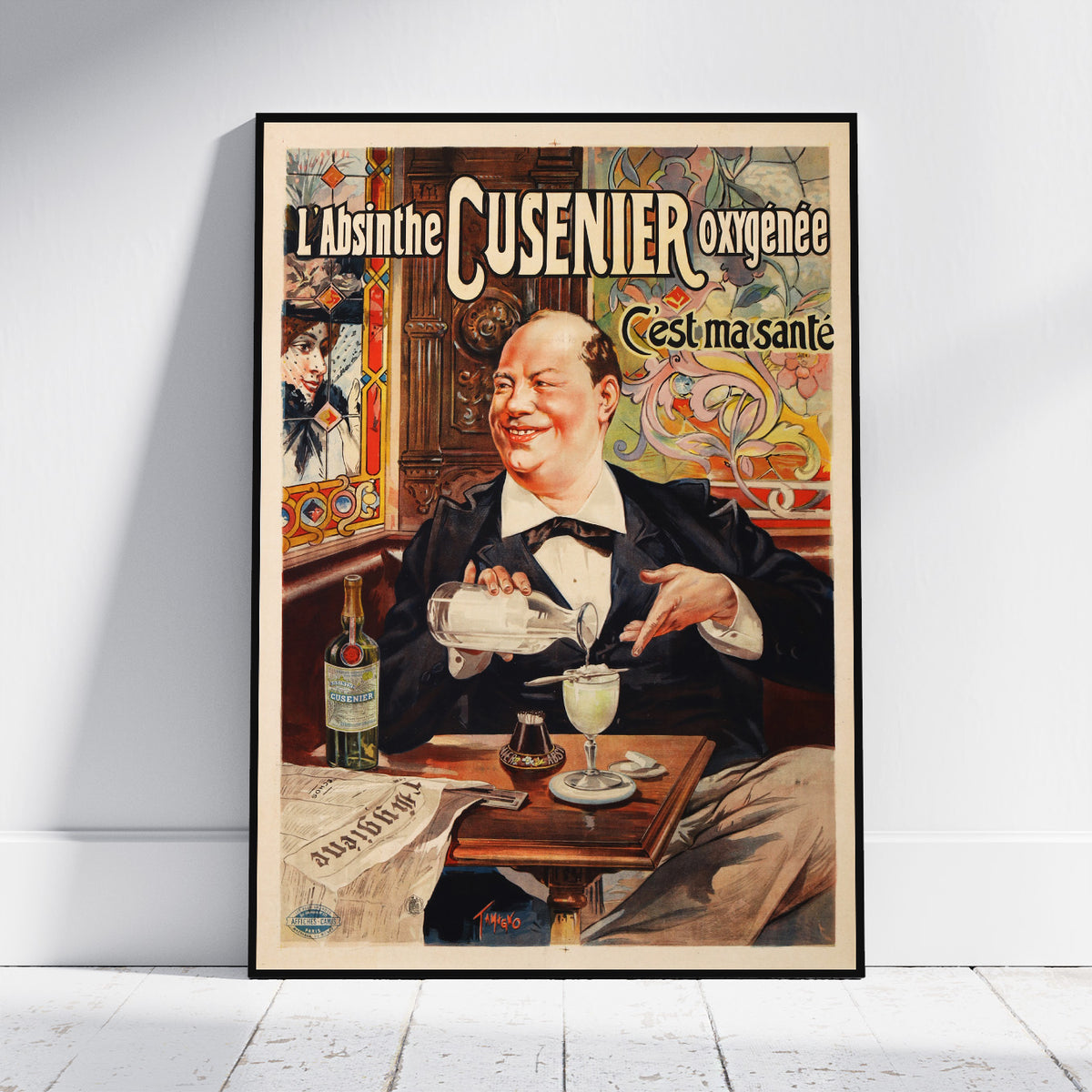 A framed vintage-style poster leaning against a white wall on a light floor. The poster features an illustrated man in a black suit pouring a drink at a table, with French text reading 'L'Absinthe CUSENIER oxygénée' and 'C'est ma santé'.