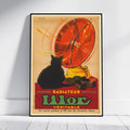 A framed vintage-style poster leaning against a white wall on a light floor. The poster shows a black cat in front of a large red radiator or fan-like object with yellow accents and bold text reading 'Essence Radiateur Petrole Ulor Veritable.