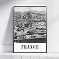 A framed black and white vintage-style poster of Marseille, France, leaning against a white wall on a light wooden floor.