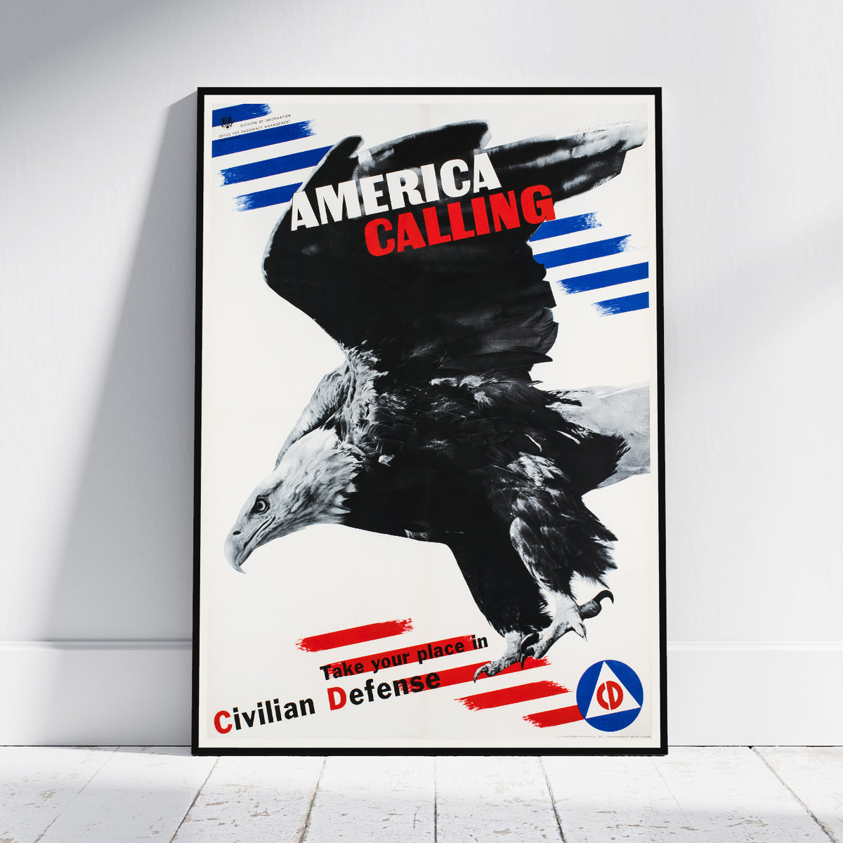 A framed vintage-style poster leaning against a white wall on a light wood floor. The poster features a large black-and-white eagle with bold text reading 'AMERICA CALLING' and 'Take your place in Civilian Defense,' plus blue and red graphic accents.