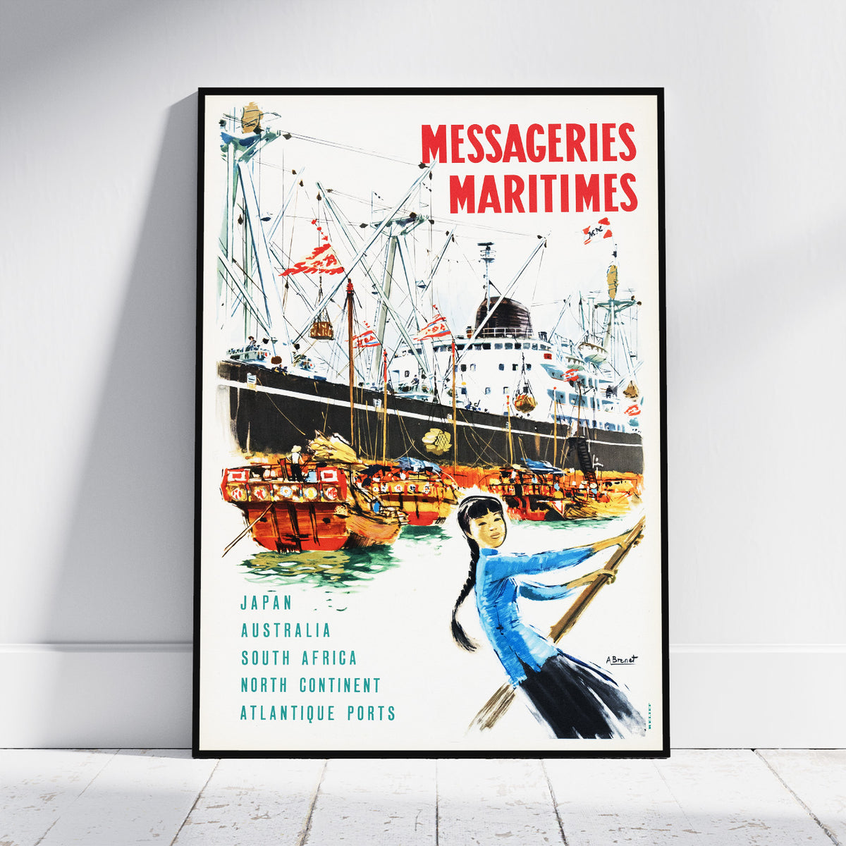 A framed vintage-style travel poster leaning against a white wall on a light wood floor. The poster features the text 'MESSAGERIES MARITIMES' in red at the top, an illustration of large cargo ships and smaller boats in a harbor, and a woman in a blue top in the lower right.