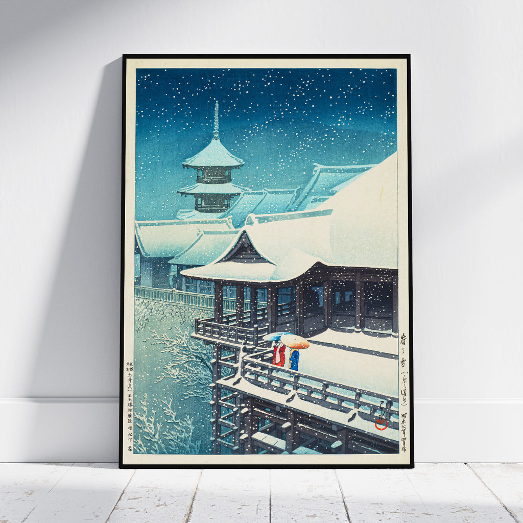 A framed art print depicting a traditional Japanese snow scene leaning against a white wall on a light wood floor.
