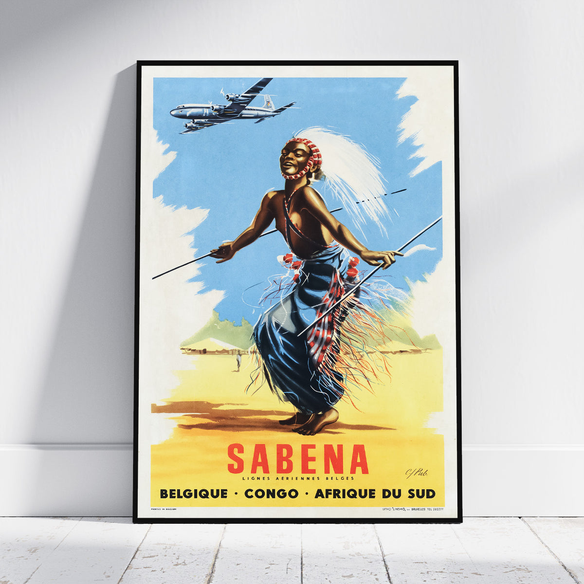 A framed vintage-style travel poster leaning against a white wall on a light wood floor. The poster shows a dancer in blue and red garments under a blue sky with an airplane overhead, and the large word 'SABENA' with smaller text 'Belgique • Congo • Afrique du Sud' at the bottom.