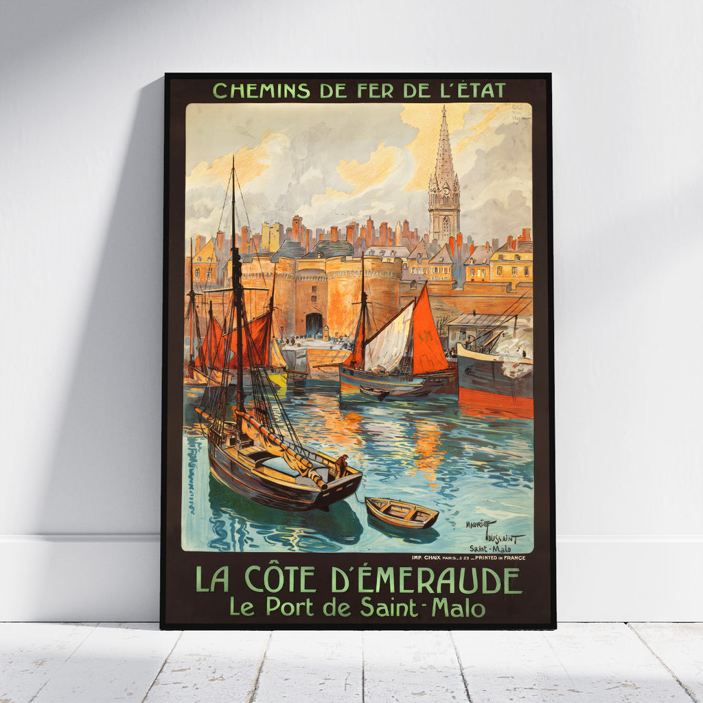 A framed vintage-style travel poster leaning against a white wall on a light floor. The artwork shows a coastal harbor scene with sailboats, a city skyline, and a church spire, with French text reading 'CHEMINS DE FER DE L'ETAT' at the top and 'LA COTE D'EMEAUDE Le Port de Saint-Malo' at the bottom.