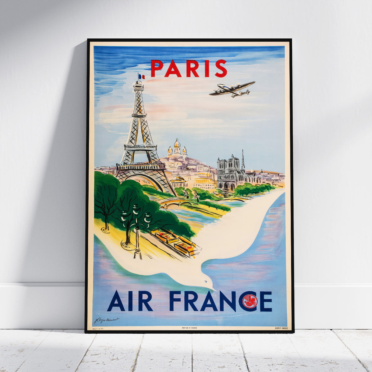 A framed vintage-style Paris travel poster leaning against a white wall on a light floor. The poster features the Eiffel Tower, Seine river, Paris skyline, an airplane, and large text reading 'PARIS' and 'AIR FRANCE'.