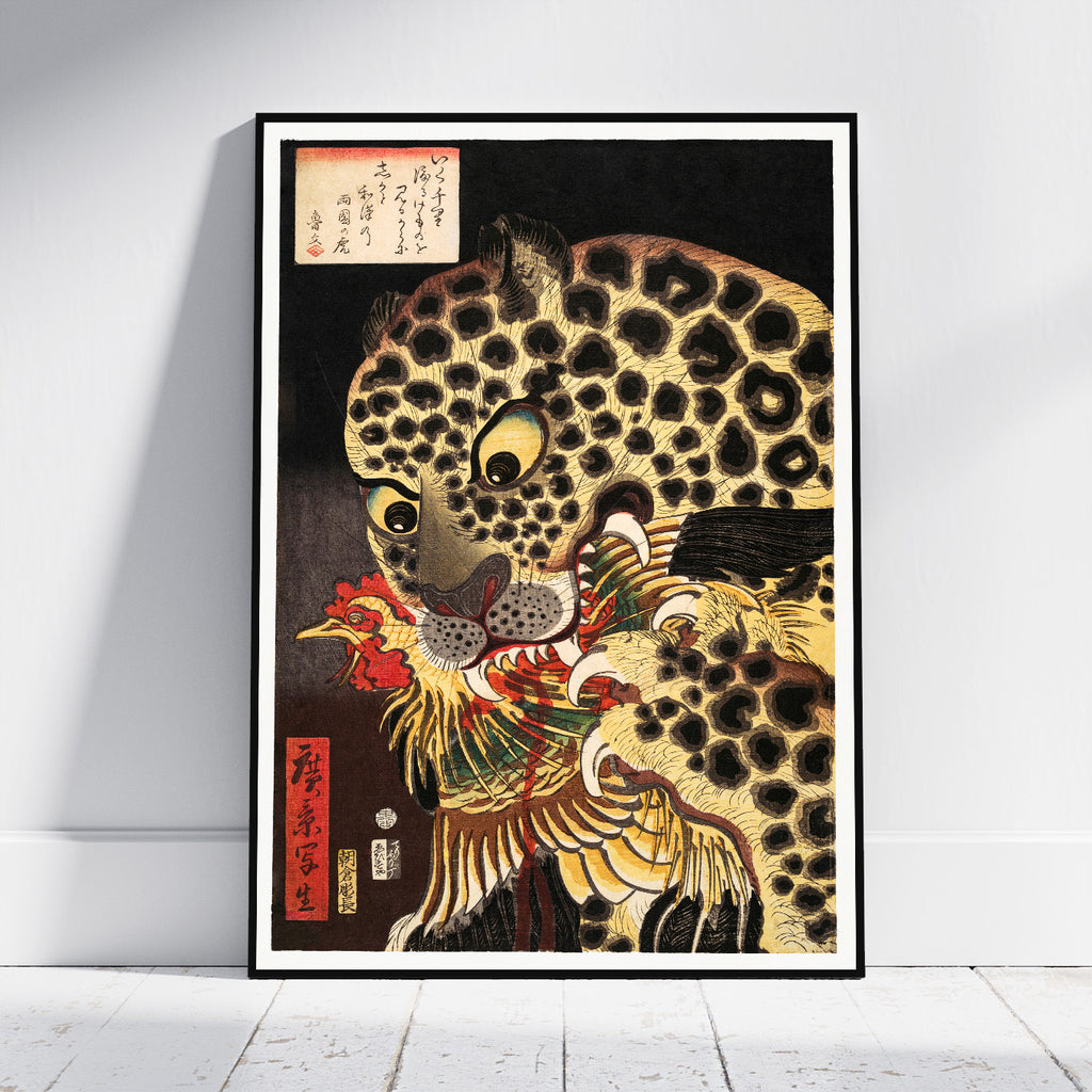 A framed Japanese-style art print leaning against a white wall on a light floor. The artwork shows a large spotted leopard or cat in profile with a red bird in its mouth, rendered in black, gold, cream, and red tones with Japanese calligraphy in the upper left and a red vertical label near the lower left.