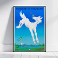 A framed travel poster featuring a whimsical white horse jumping against a bright blue sky, with the text 'VACANZE IN SVIZZERA' at the top and a small Swiss flag near the bottom. The poster is displayed leaning against a white wall on a light wood floor.