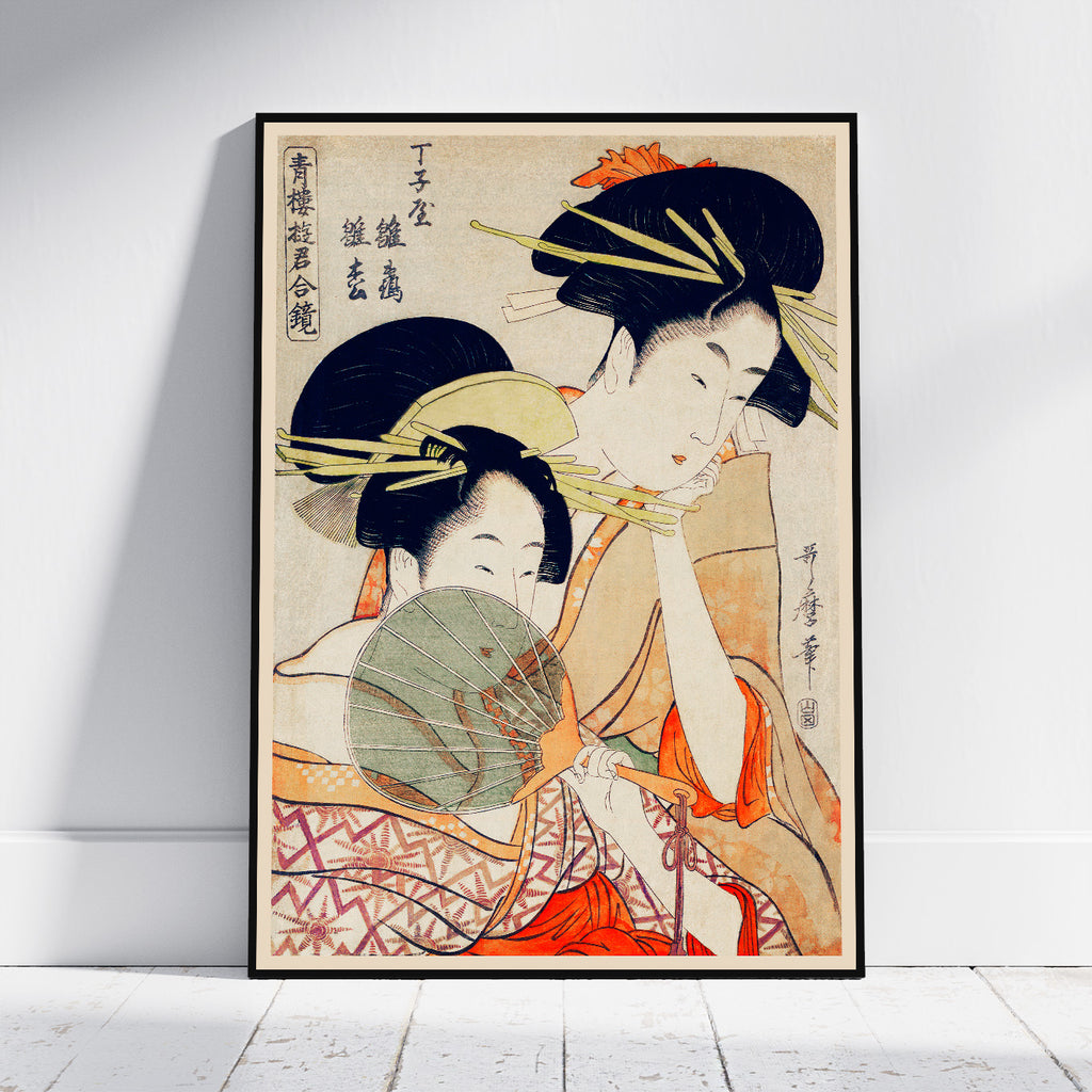 A framed Japanese ukiyo-e woodblock print depicting two women in traditional attire, leaning against a white wall on a light wood floor.