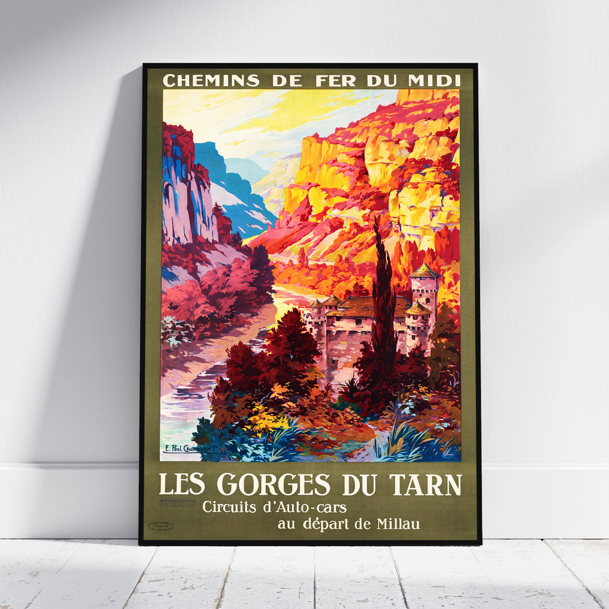 A framed vintage-style travel poster leaning against a white wall on a light floor. The poster depicts a colorful mountain landscape with cliffs, trees, and buildings, with French text reading 'CHEMINS DE FER DU MIDI' at the top and 'LES GORGES DU TARN' at the bottom.