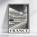 A framed black and white vintage-style travel poster of Chantilly, France, leaning against a white wall on a light wood floor.