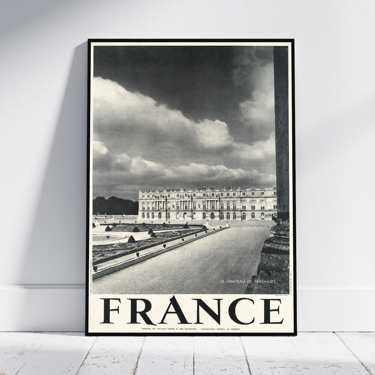 A framed black and white vintage-style travel poster of Chantilly, France, leaning against a white wall on a light wood floor.