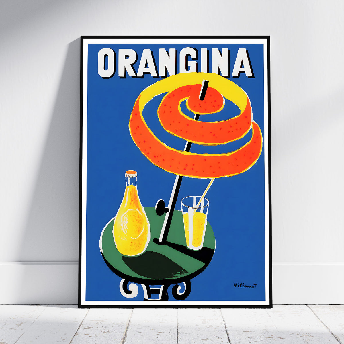 A framed vintage-style poster leaning against a white wall on a light floor. The poster shows the word "ORANGINA" at the top, with a large spiral orange peel under a black umbrella, a yellow-orange bottle, and a glass of orange drink on a blue background.