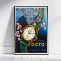 A framed vintage-style watch poster leaning against a white wall on a light wood floor. The artwork shows a gold-tone wristwatch with a green strap, pink cherry blossoms, a dark pagoda silhouette, and the text 'OCTO BIENNE (SWITZERLAND)'.