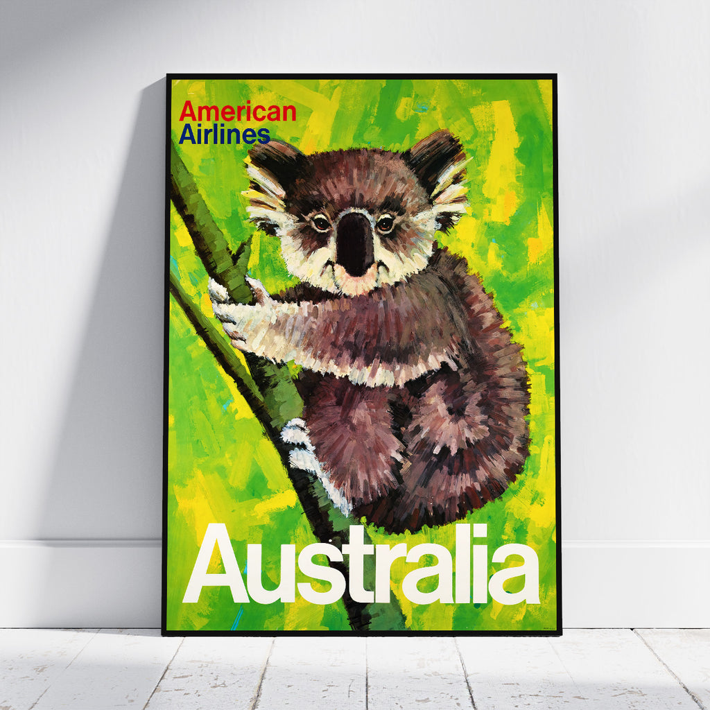 A framed travel poster featuring a painted koala on a bright green and yellow background, with the text 'American Airlines' at the top and 'Australia' at the bottom, leaning against a white wall on a light floor.