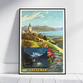 A framed vintage travel poster of Lac Léman, Quebec, leaning against a white wall on a light wood floor. The poster features a colorful illustration of a scenic lake landscape with mountains, a train, and pink flowers in the foreground, with 'LAC LÉMAN' printed in bold yellow letters at the bottom.