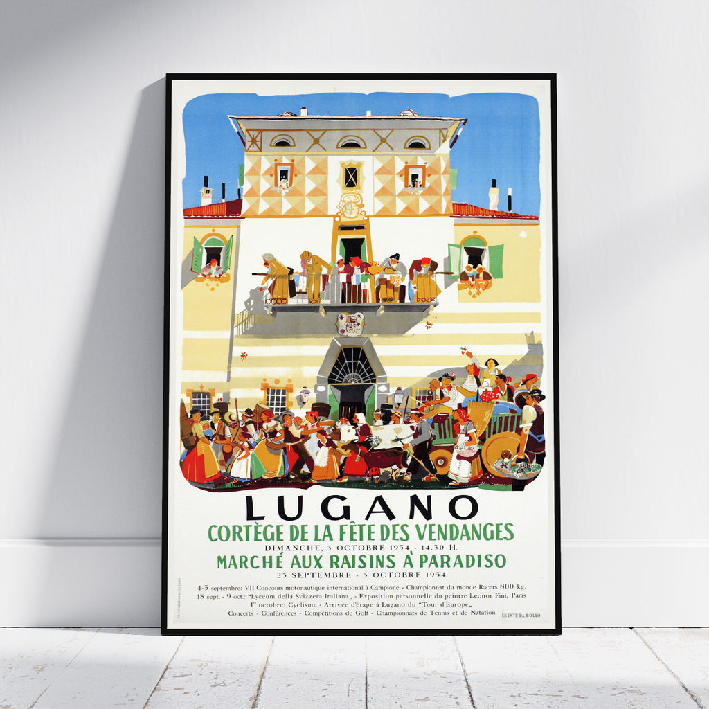 A framed vintage-style travel poster leaning against a white wall on a light wood floor. The poster features an illustration of a grand building facade with dancing figures on balconies and a large crowd gathered below, with the text 'LUGANO' and French event details.