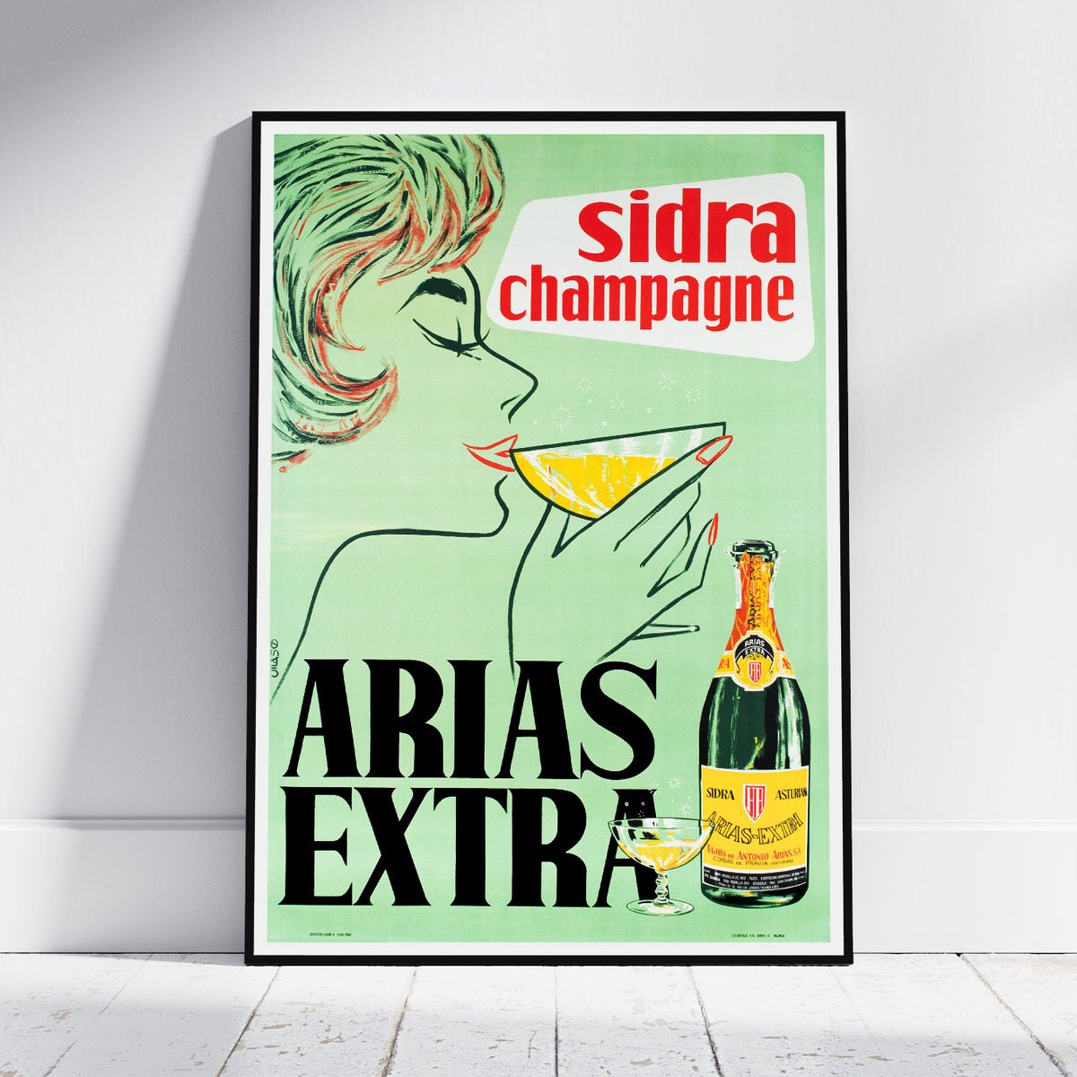 A framed vintage-style advertising poster for ARIA'S EXTRA sidra champagne leaning against a white wall on a light floor. The poster features a woman drinking from a glass, a champagne bottle, and bold text reading 'sidra champagne' and 'ARIA'S EXTRA' on a pale green background.