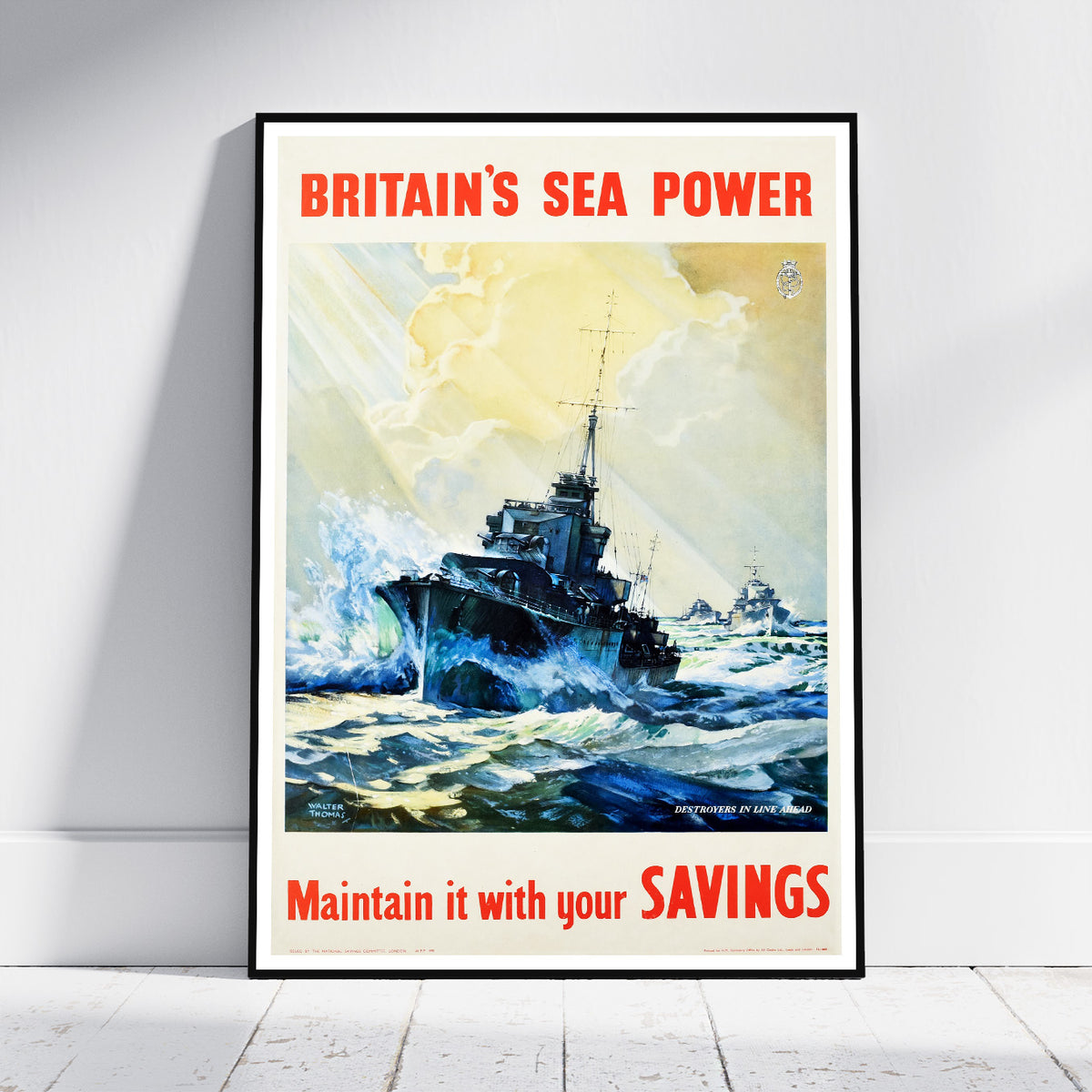 A framed vintage-style poster leaning against a white wall on a light floor. The poster artwork shows two navy warships at sea with large red text reading “BRITAIN'S SEA POWER” at the top and “Maintain it with your SAVINGS” at the bottom.