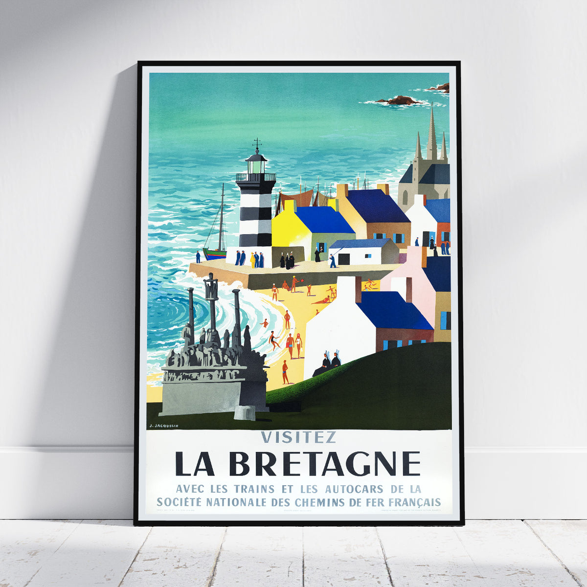 A framed vintage-style travel poster leaning against a white wall on a light floor. The poster depicts a coastal seaside town with a lighthouse, blue ocean, colorful buildings, and the French text 'VISITEZ LA BRETAGNE' at the bottom.