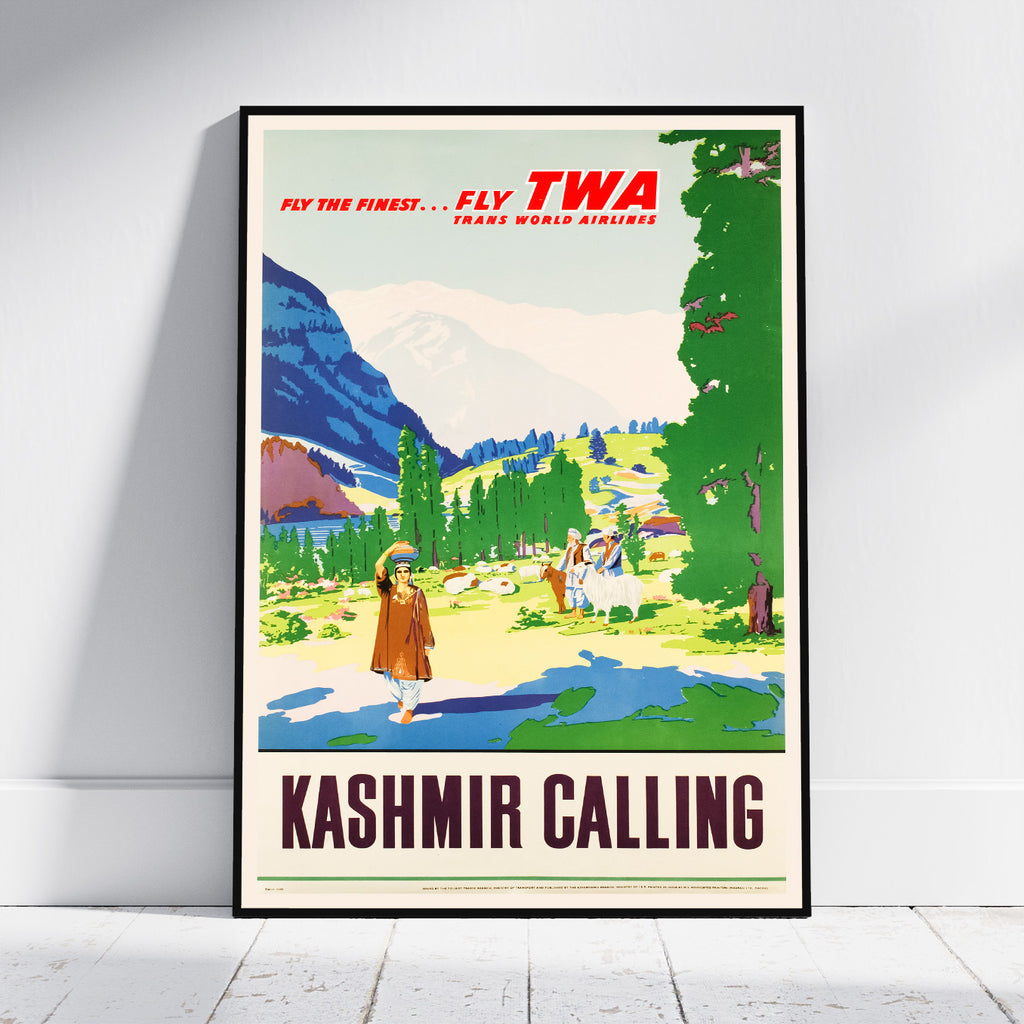 A framed vintage-style travel poster leaning against a white wall on a light floor. The poster reads 'KASHMIR CALLING' and features a colorful illustrated landscape with mountains, trees, and figures, plus 'FLY TWA TRANS WORLD AIRLINES' text at the top.