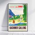 A framed vintage-style travel poster leaning against a white wall on a light floor. The poster reads 'KASHMIR CALLING' and features a colorful illustrated landscape with mountains, trees, and figures, plus 'FLY TWA TRANS WORLD AIRLINES' text at the top.